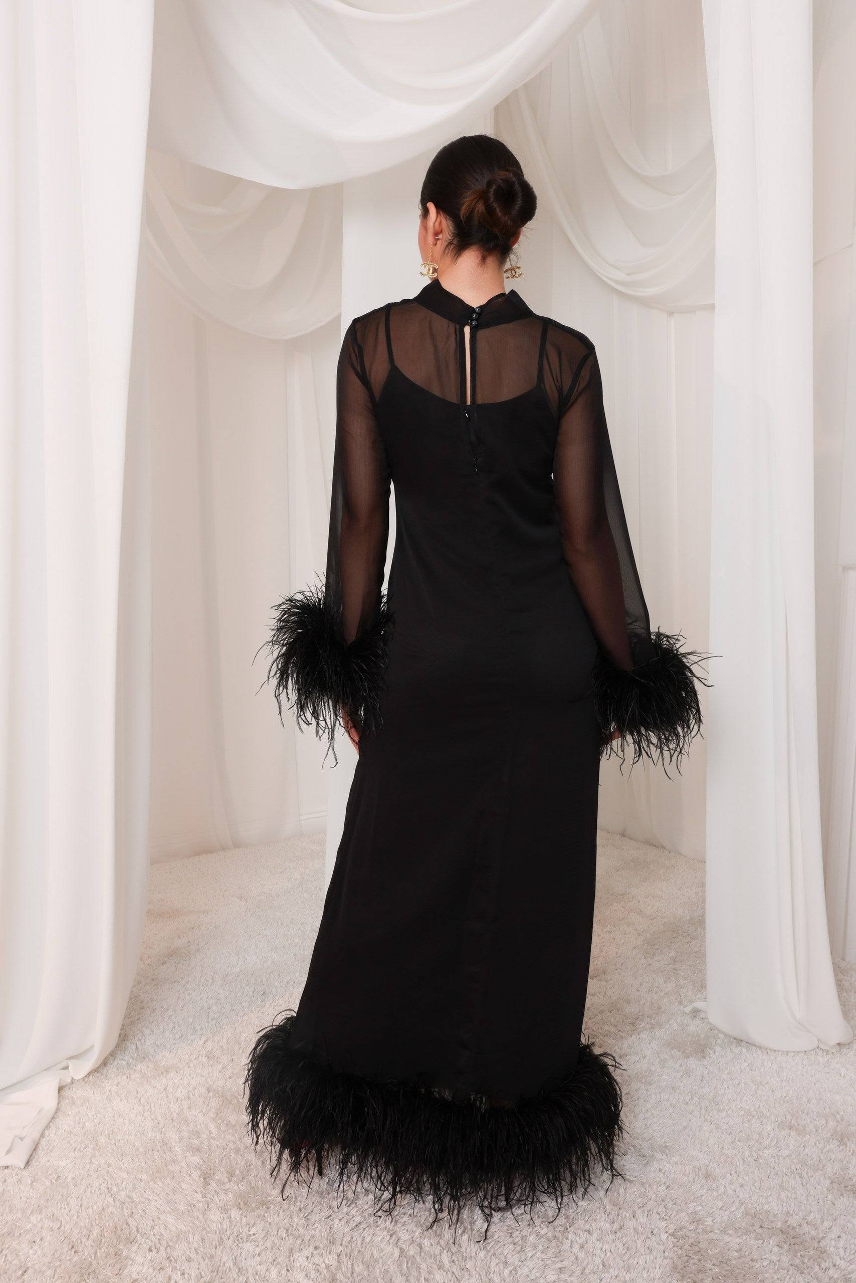 Back view of the Leila black evening gown showcasing sheer paneling, feather-trimmed sleeves, and hem. A refined choice for evening elegance.