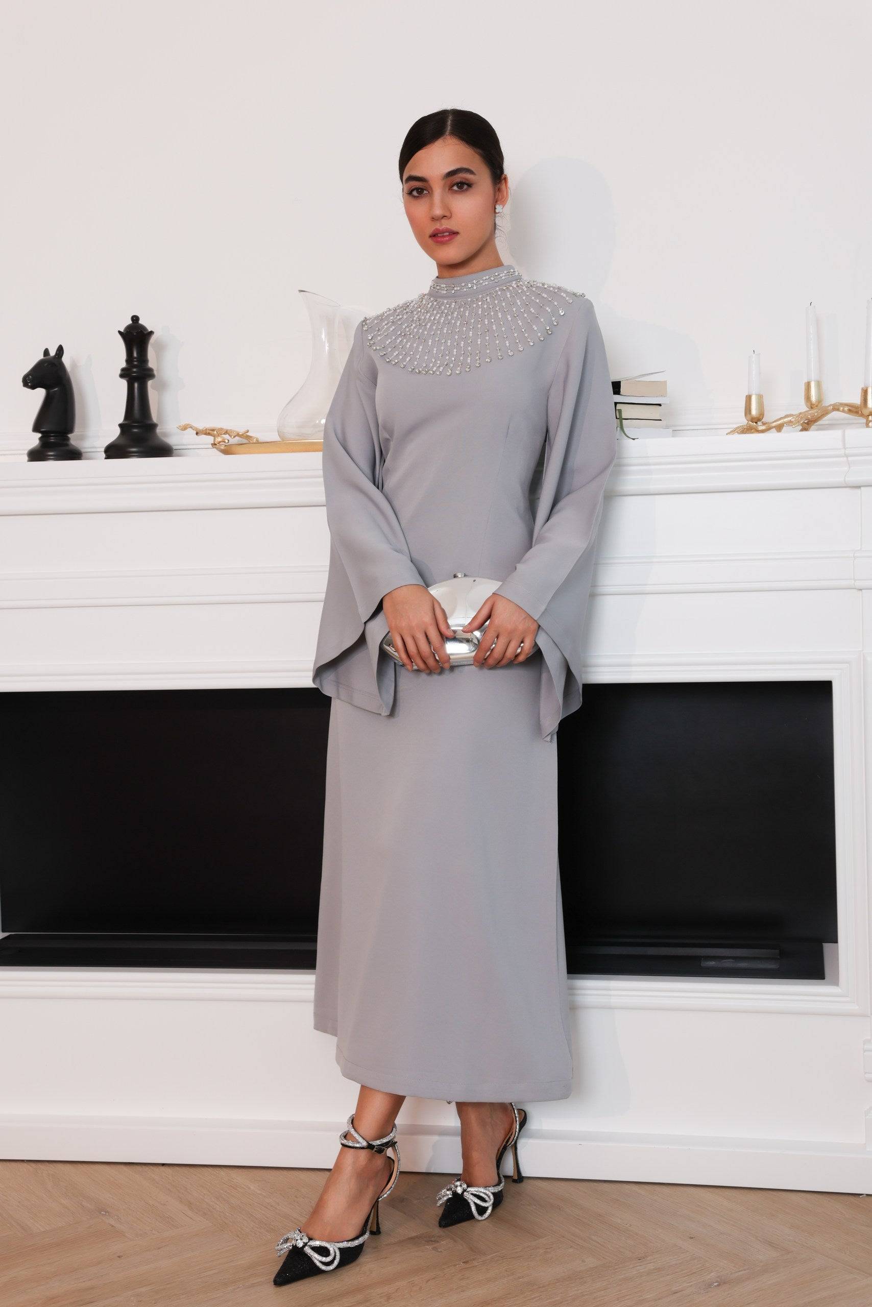 Durrah elegant dress in soft gray with a tailored fit. Features a high neckline adorned with pearl-like embellishments and flowing sleeves for timeless sophistication.